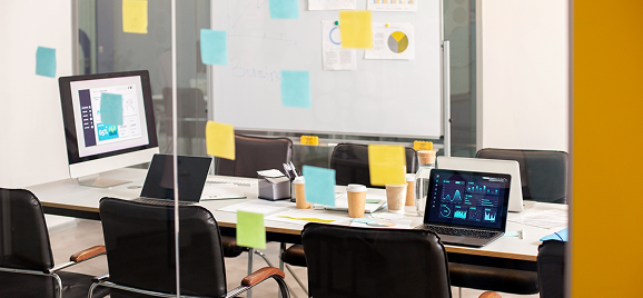 Glass-walled meeting room with sticky notes and laptops