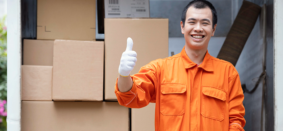 Delivery worker giving a thumbs-up beside packed furniture boxes